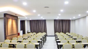 Un salón de conferencias con filas de mesas y sillas, un panel de madera en la pared y una puerta con un letrero.