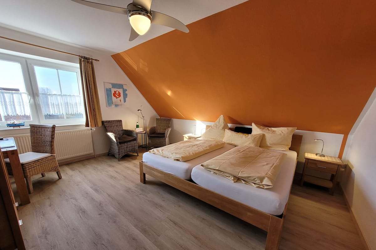 A bedroom with a large bed, two bedside tables, a chair, a desk, and a window with curtains.