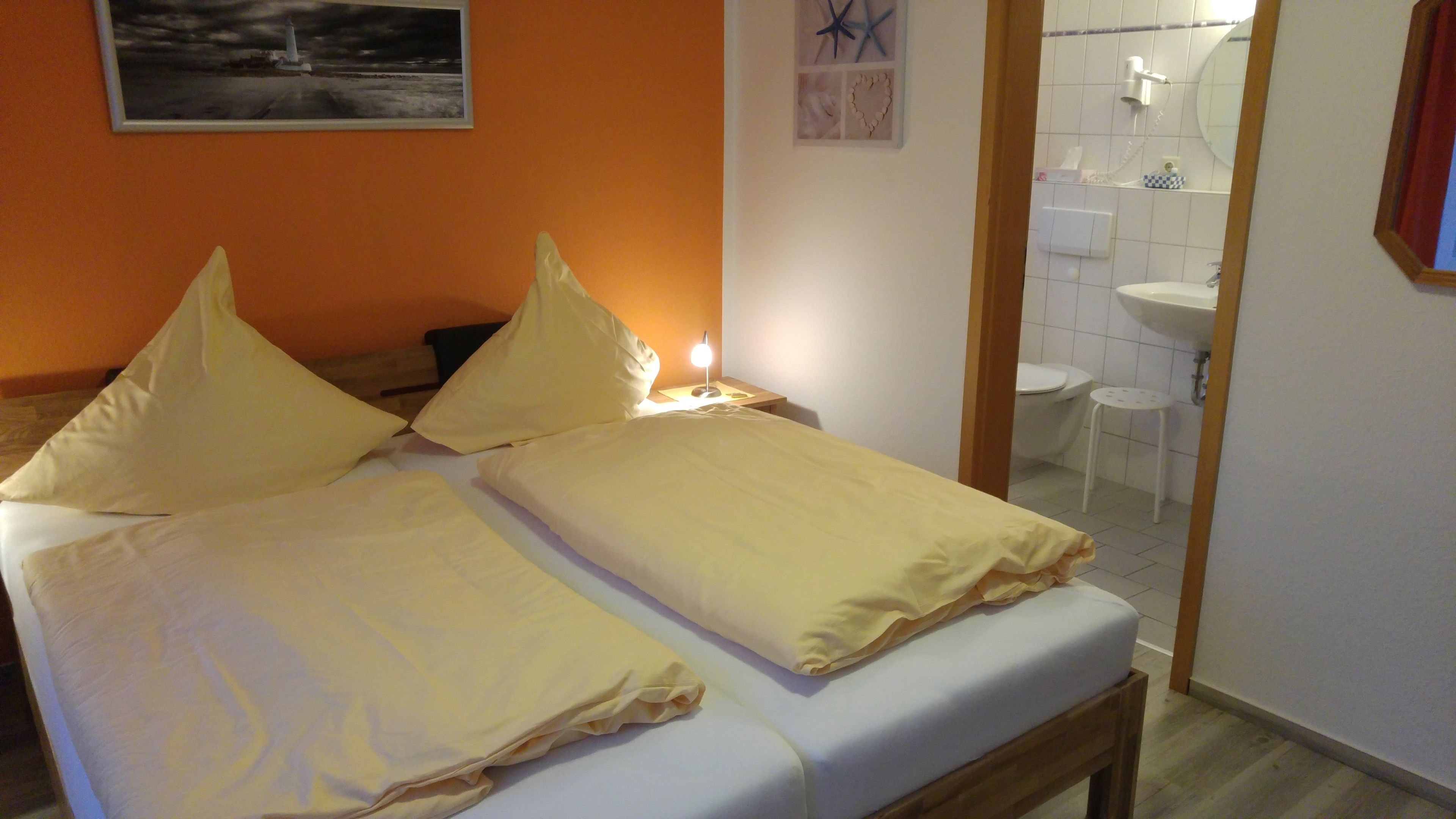 A room with a bed, a nightstand, a lamp, and a bathroom visible through an open door.