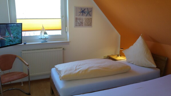 A bedroom with a bed, a chair, a nightstand with a lamp, a wall art piece, and a window with blinds.
