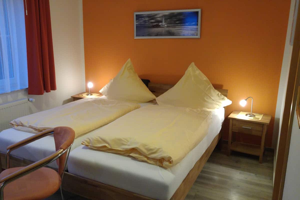 A double bed with white linens, two bedside tables with lamps, a chair, and a window with curtains.