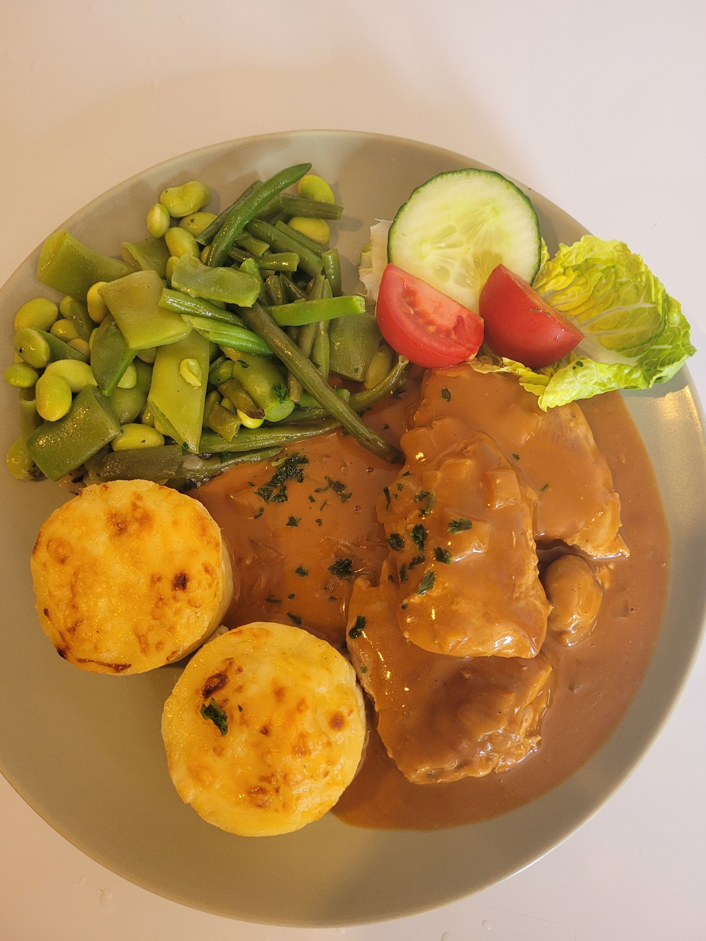 A plate of food with a meat dish, green beans, tomatoes, cucumber, and potatoes.