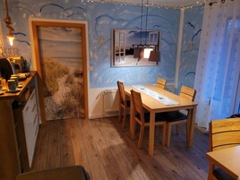 Un comedor con mesa y sillas de madera, vista a la playa a través de una puerta y un mural en el techo con anclas.