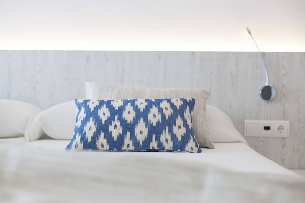 Een bed met witte beddengoed en een kussen met een blauw patroon.