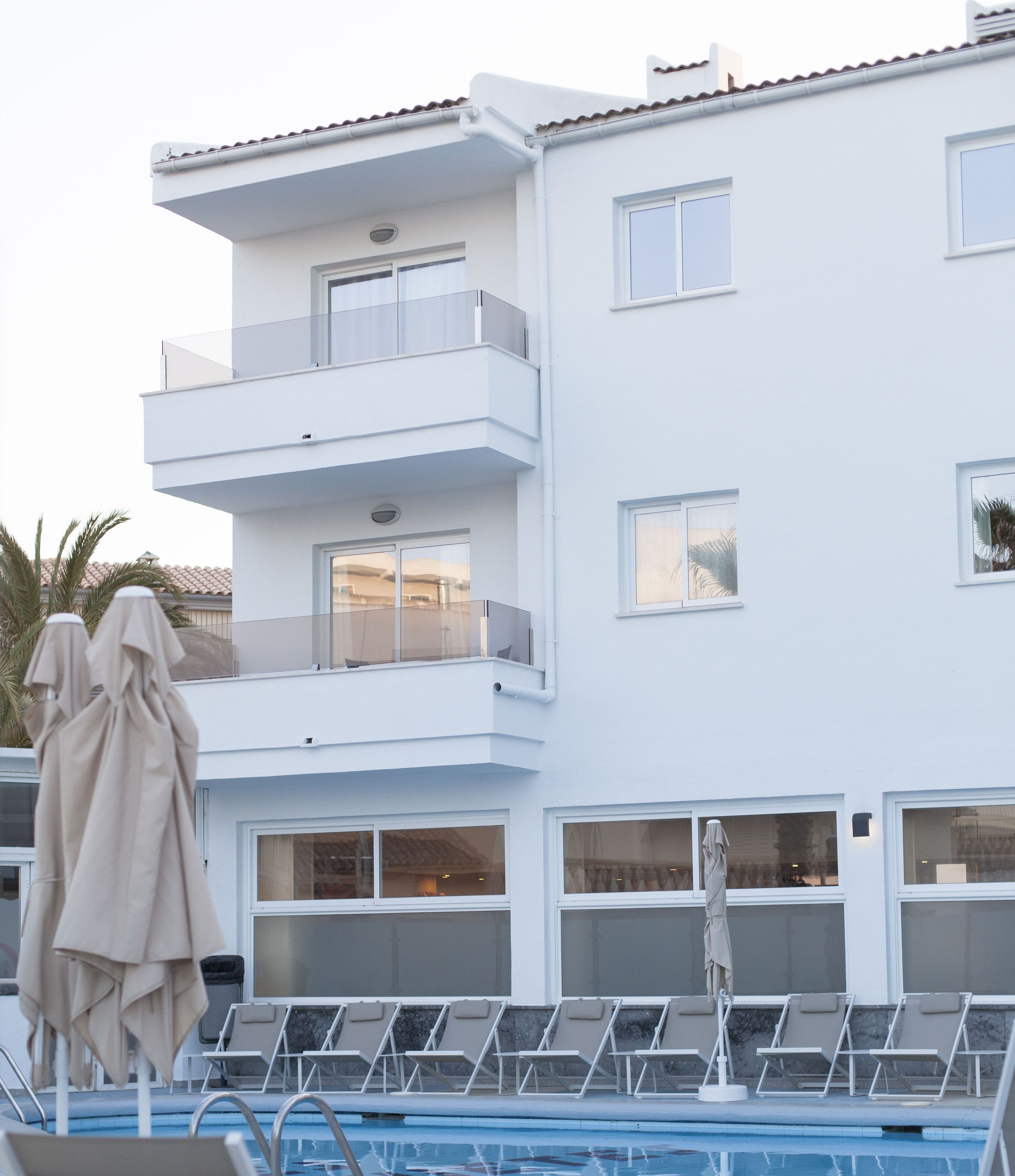 Un edificio moderno con piscina, varios balcones y sillones de descanso.