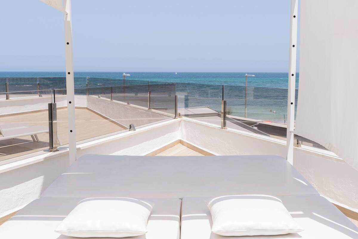 Een balkon met helder uitzicht op de oceaan, een wit gestoffeerde zithoek en een glazen balustrade.