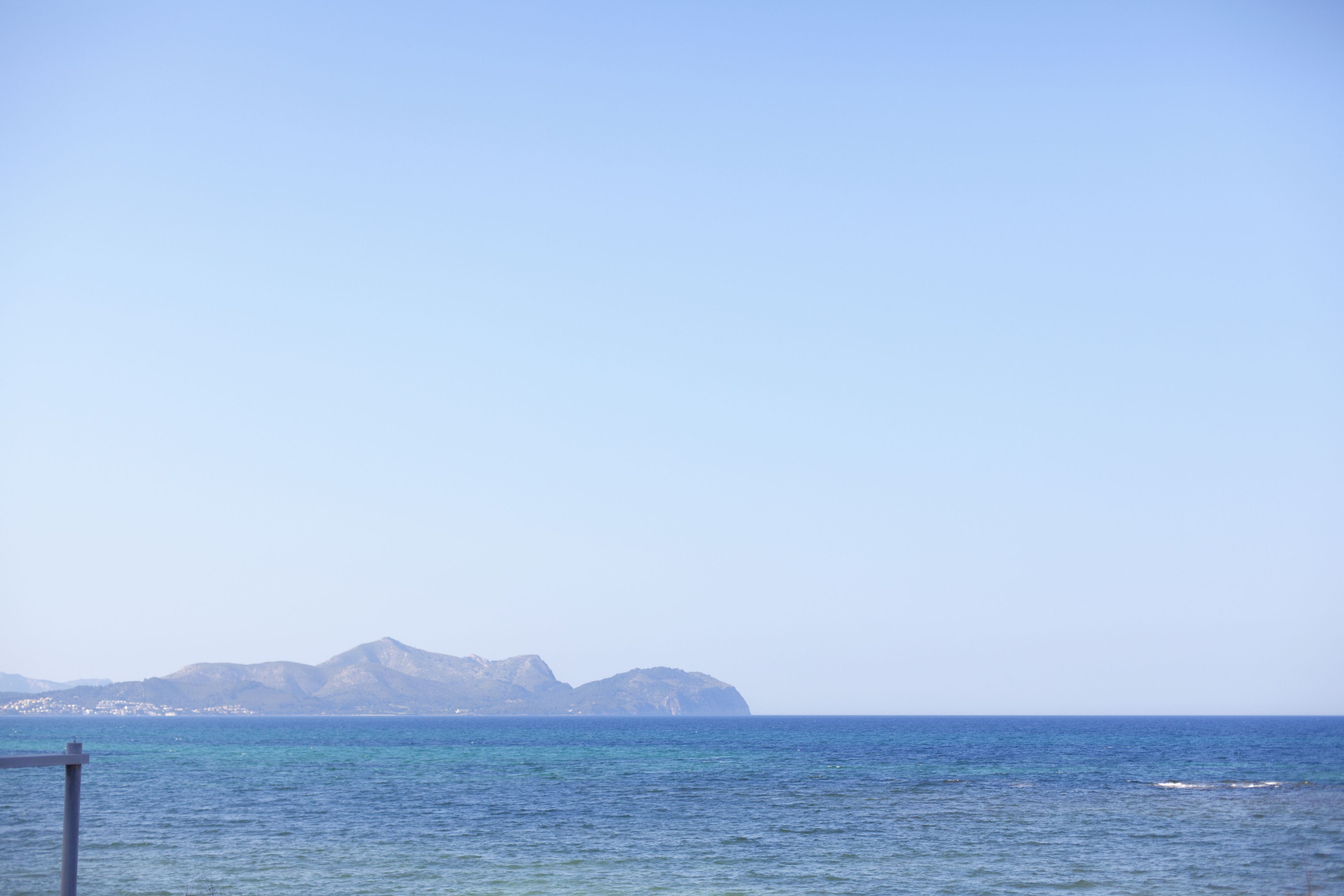 Vista costera con mar en calma y montañas a lo lejos.