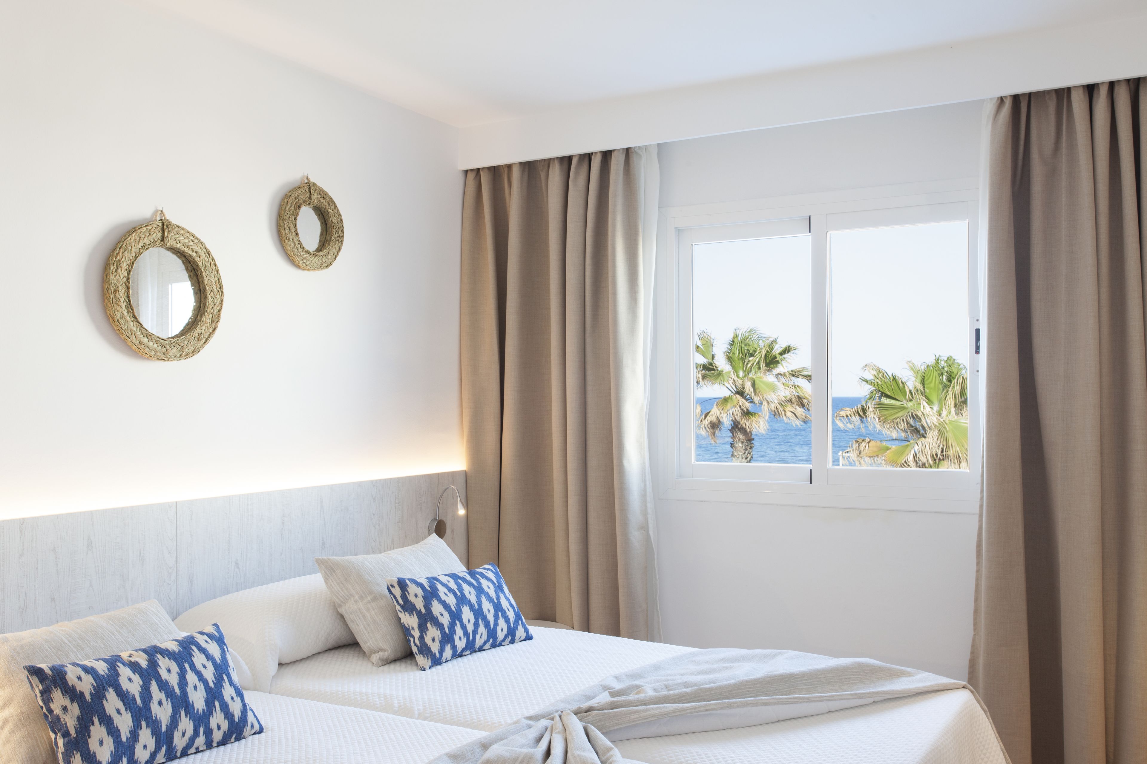 Habitación de hotel con una cama, dos almohadas, una ventana con cortinas y dos espejos en la pared.