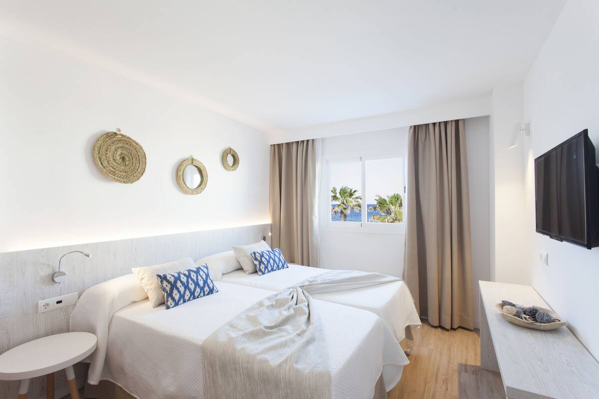 Een hotelkamer met twee bedden, een ronde tafel, een televisie en een raam met gordijnen.