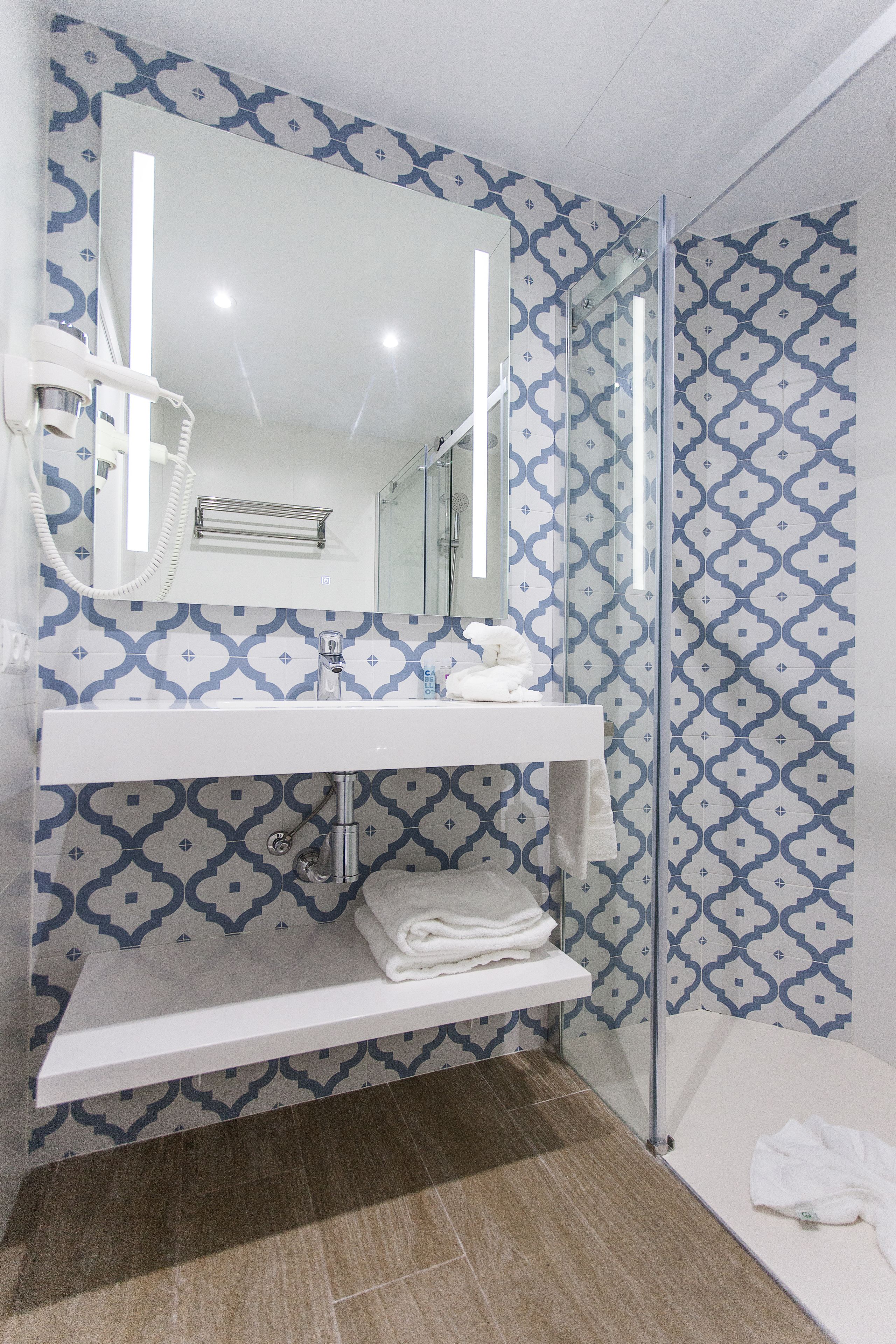 Un baño con pared estampada, un lavamanos blanco, un espejo y una cabina de ducha de vidrio.