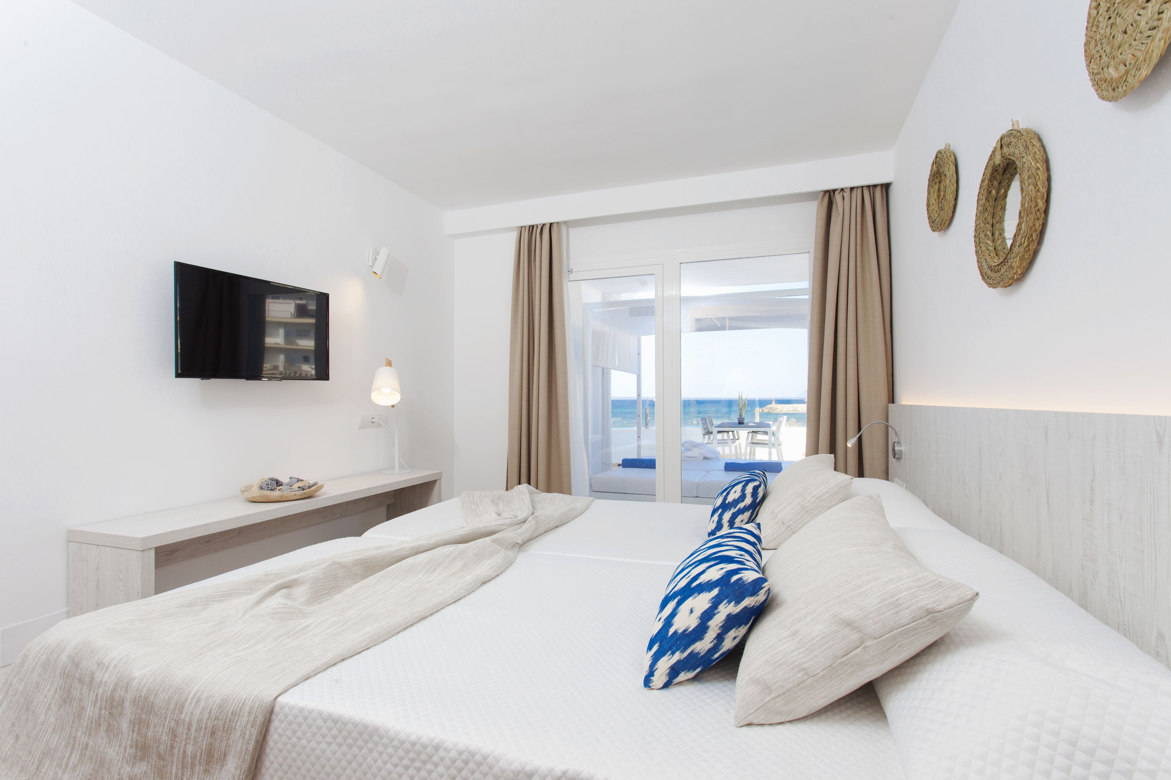 A hotel room with a bed, a TV, a bedside table, and a view of the sea through a glass door.