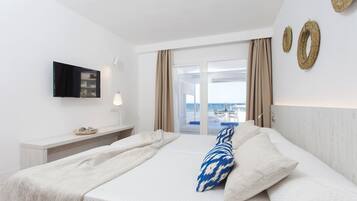 A hotel room with a bed, a TV, a bedside table, and a view of the sea through a glass door.