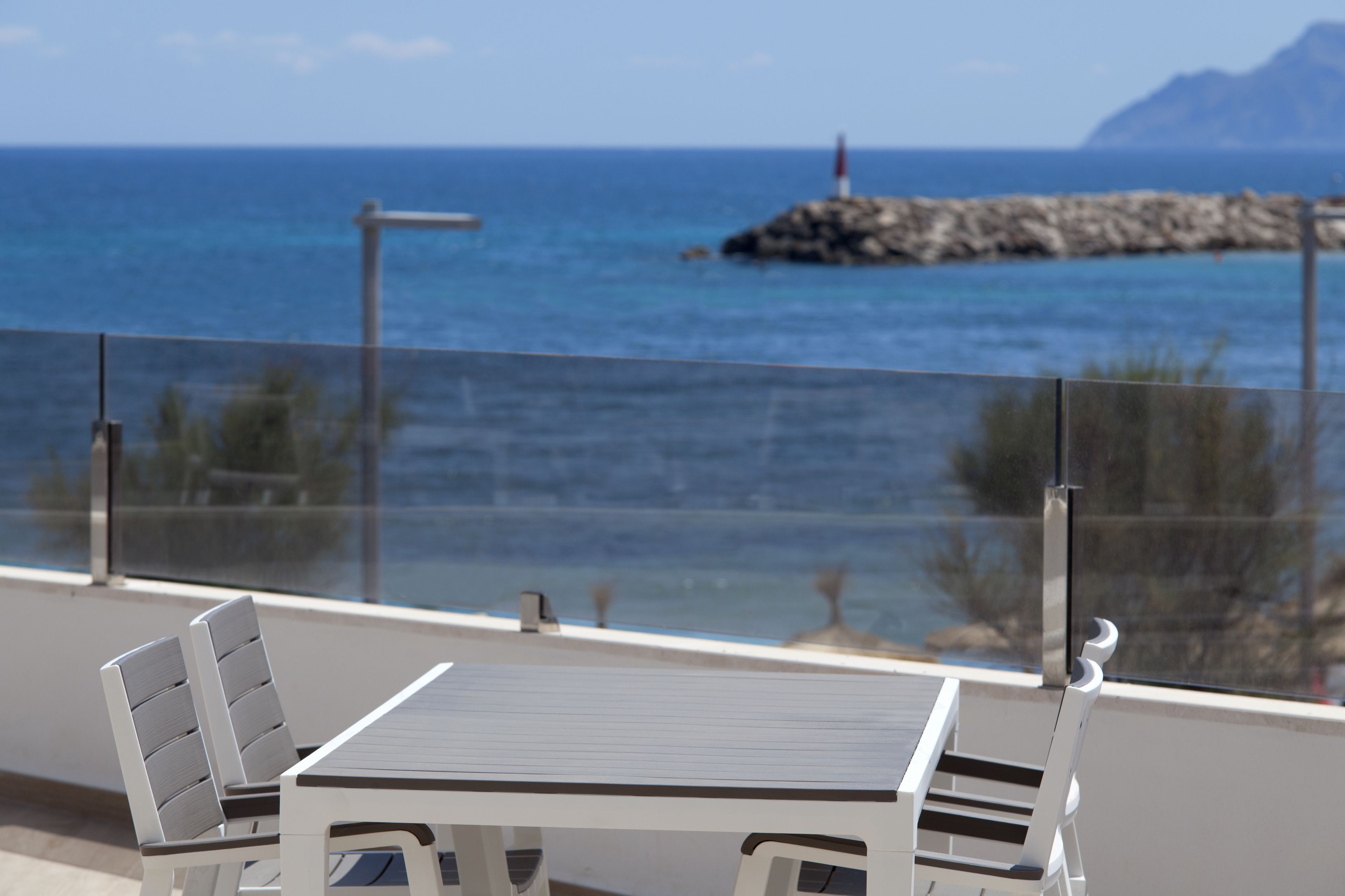 Un balcón con mesa y sillas, con vista a una costa rocosa y al mar.