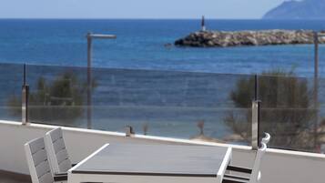 Un balcón con mesa y sillas, con vista a una costa rocosa y al mar.