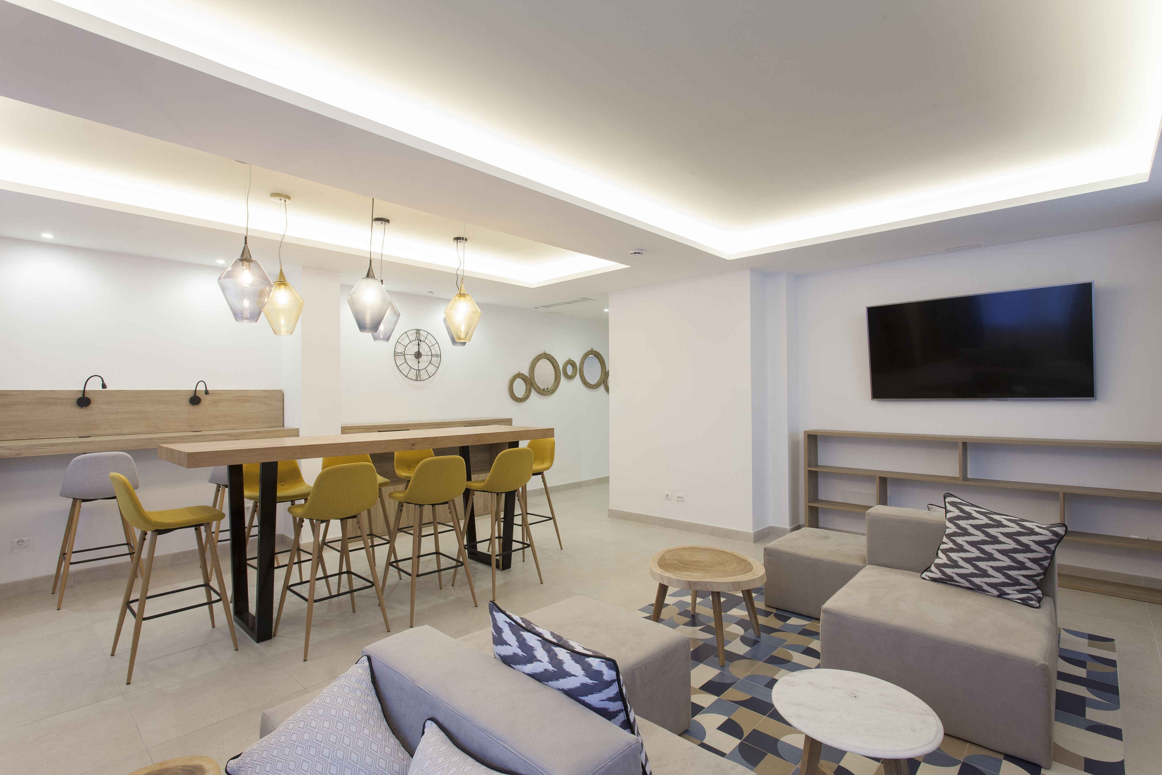 Ein modernes Wohnzimmer mit Essbereich, Sofas, einem Fernseher und Pendelleuchten.