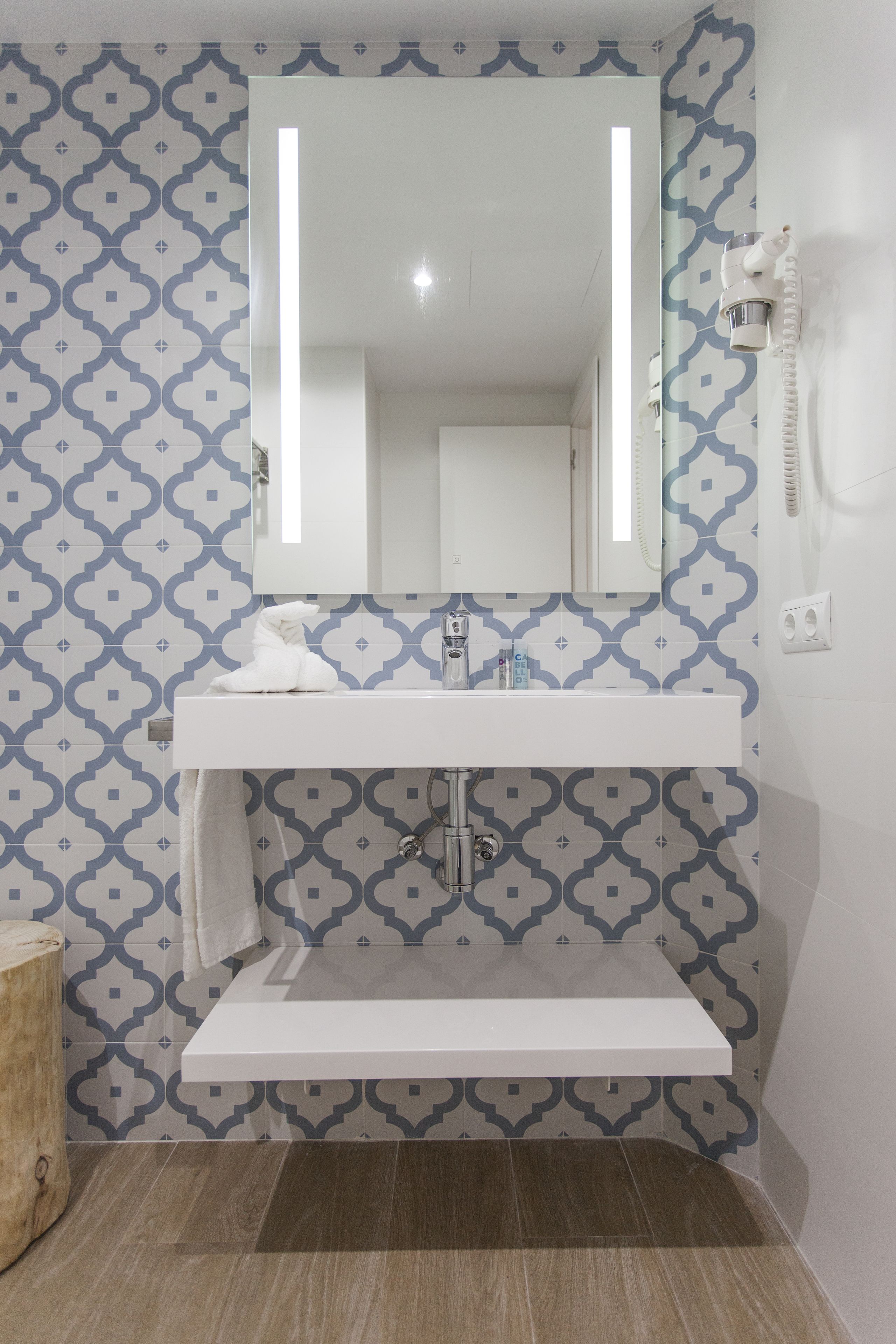 Casa de banho com lavatório branco, espelho e azulejos estampados.