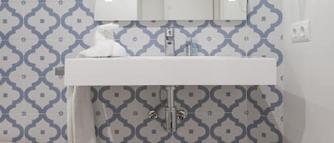 A bathroom with a white sink, a mirror, and patterned wall tiles.