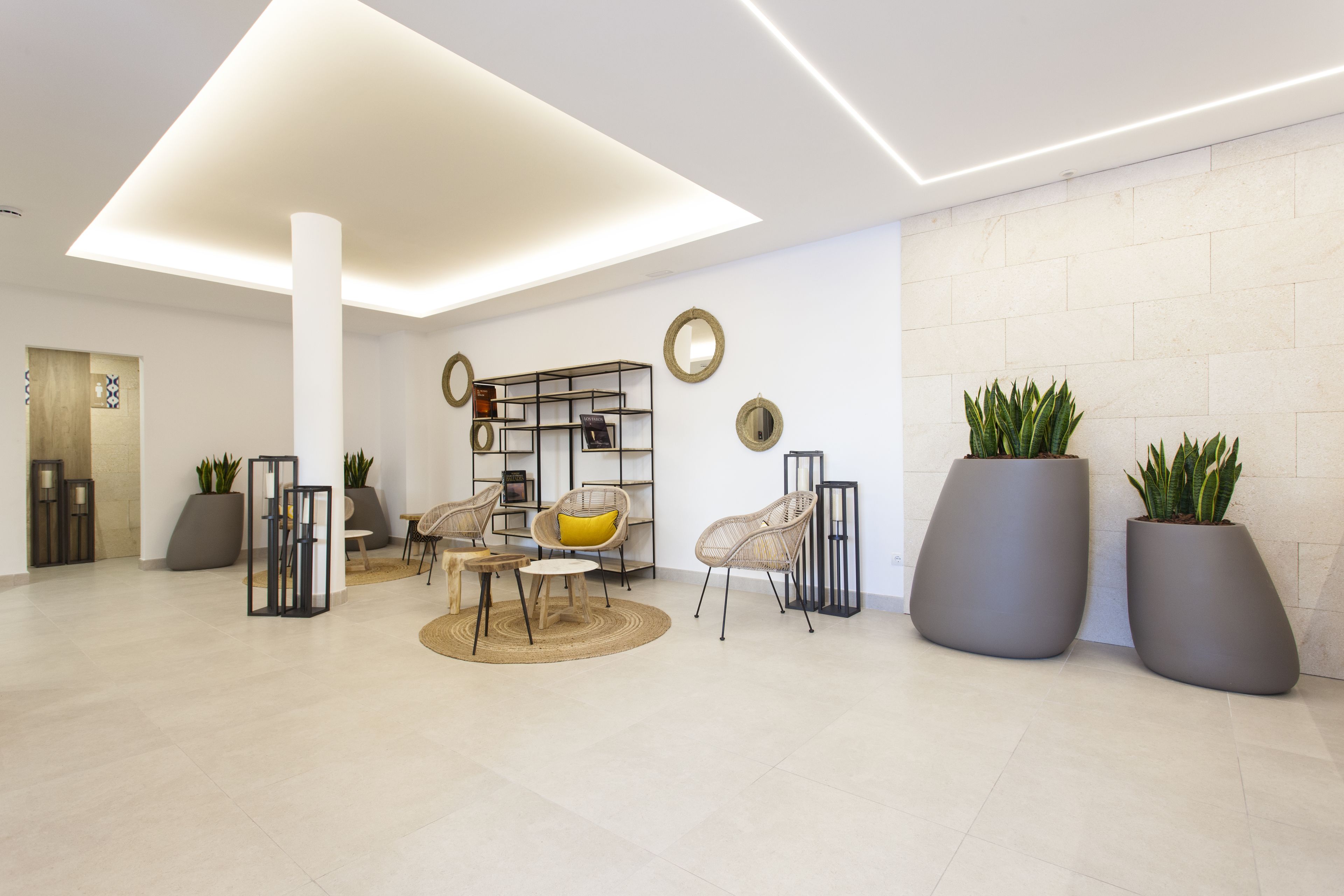 Un hall d’entrée moderne avec un espace salon central, une grande colonne blanche et des plantes en pot.
