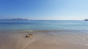 Ein Strand mit klarem Wasser, einem Felsen im Sand und Bergen in der Ferne.