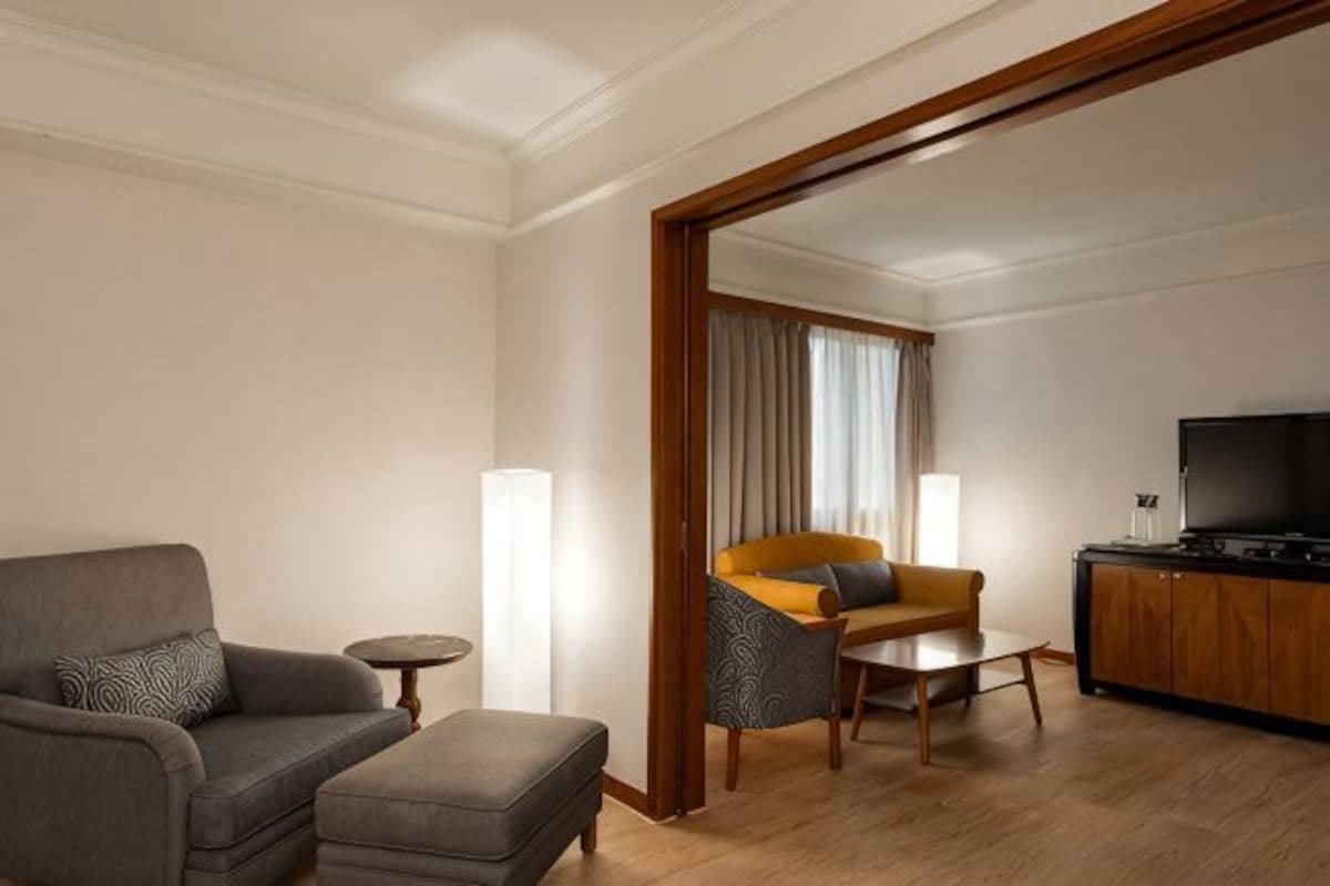 Une chambre d’hôtel équipée d’un canapé, d’un pouf, d’une petite table, d’une télévision et d’une armoire en bois.