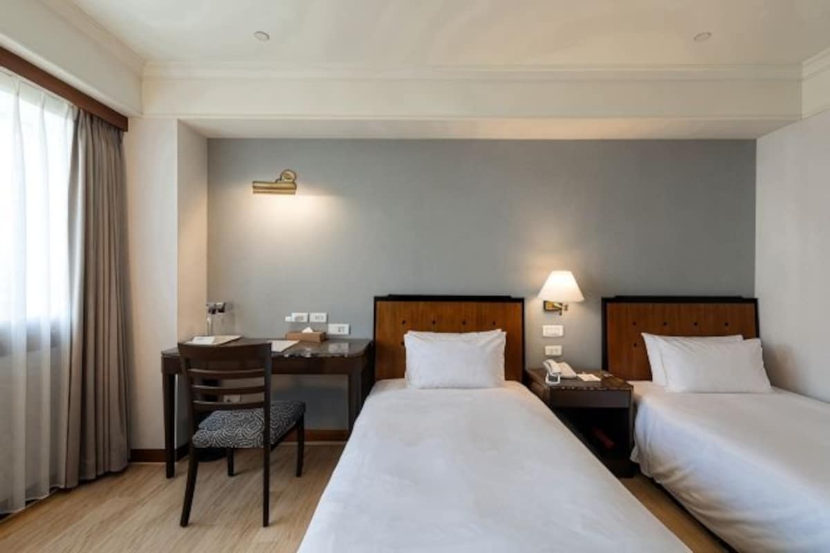 Une chambre d’hôtel avec deux lits, un bureau, une chaise et une table de chevet avec une lampe.