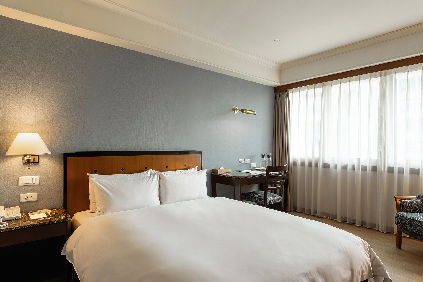 Une chambre d’hôtel avec un grand lit, un bureau avec une lampe, un téléphone et une chaise.