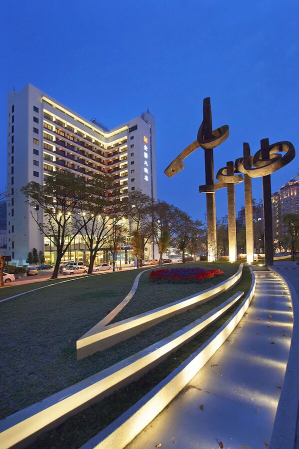 A modern hotel with multiple floors, a landscaped garden, and a distinctive metal sculpture.