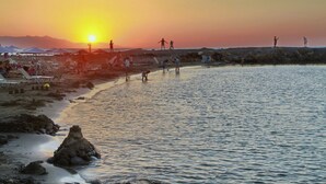 A beach scene with people enjoying the sunset, umbrellas, and lounge chairs. - Kalia Beach (Hersonissos)