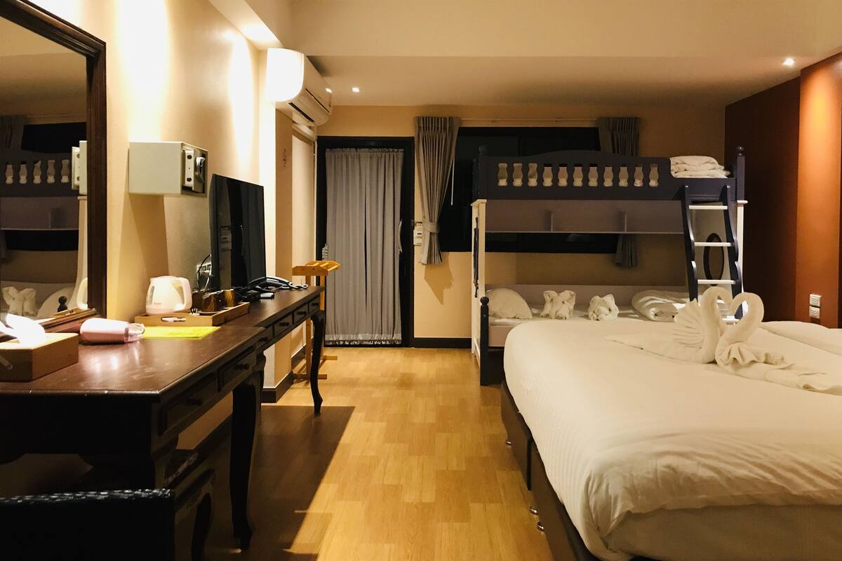 Une chambre d’hôtel avec un lit superposé, un bureau avec une chaise, un miroir, une table de chevet et une armoire.