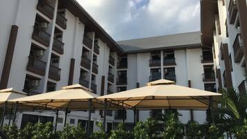 A multi-story hotel with balconies, outdoor umbrellas, and lush greenery.