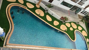 Una piscina de diseño singular, rodeada de jardines con palmeras y un solárium con tumbonas.