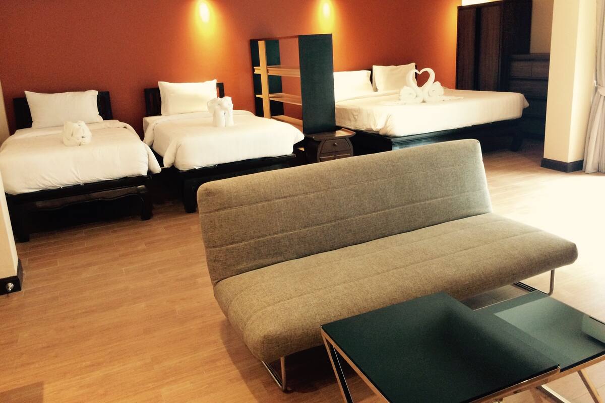 Une chambre d’hôtel avec deux lits, un canapé gris et une petite table.