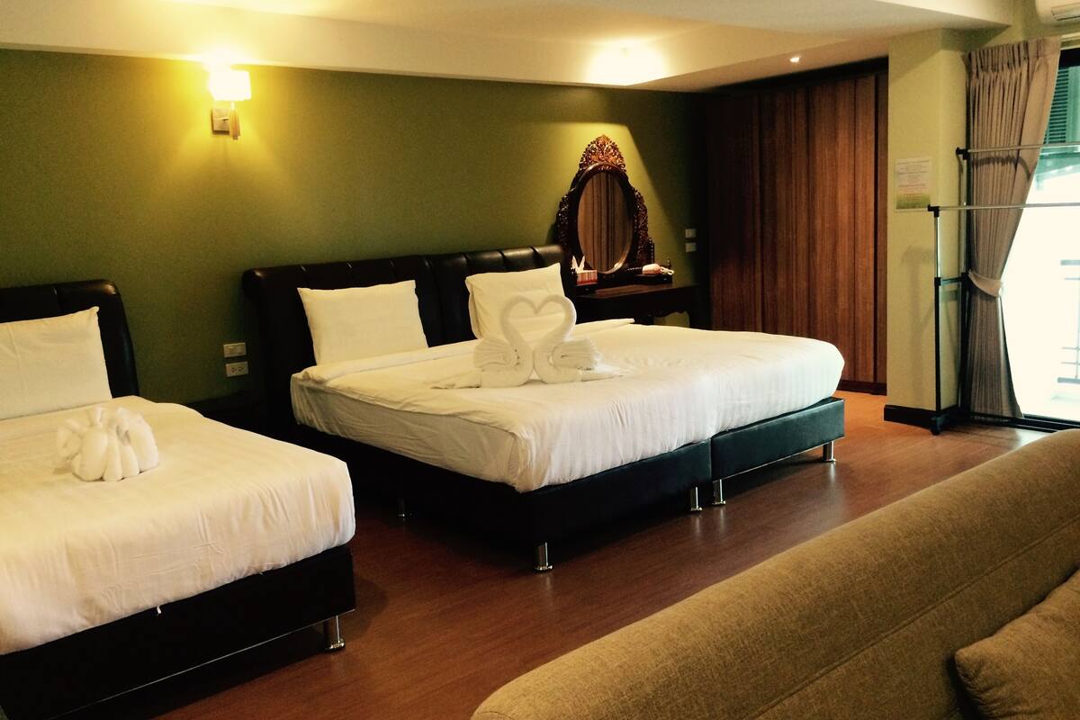 Une chambre d’hôtel avec deux lits, un canapé, un miroir et une fenêtre avec des rideaux.