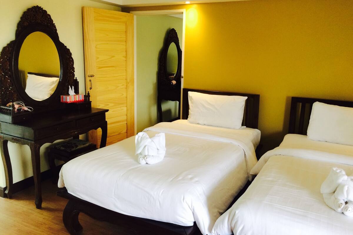 Une chambre d’hôtel avec deux lits, une commode en bois, un miroir et une porte.
