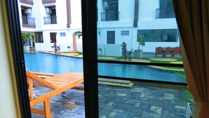 Vista de una piscina con cubierta de madera y losetas de piedra, rodeada de edificios con balcones y ventanas.