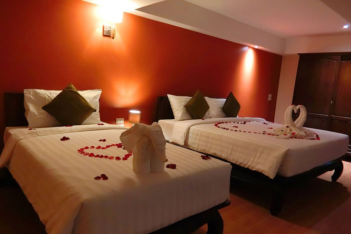 Deux lits impeccablement faits, recouverts de draps blancs, de pétales de rose et de serviettes disposées en forme de cœur sur chaque lit.