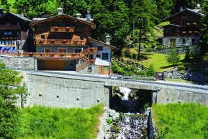 Un chalet en bois doté d’un balcon, un pont de pierre et un ruisseau.