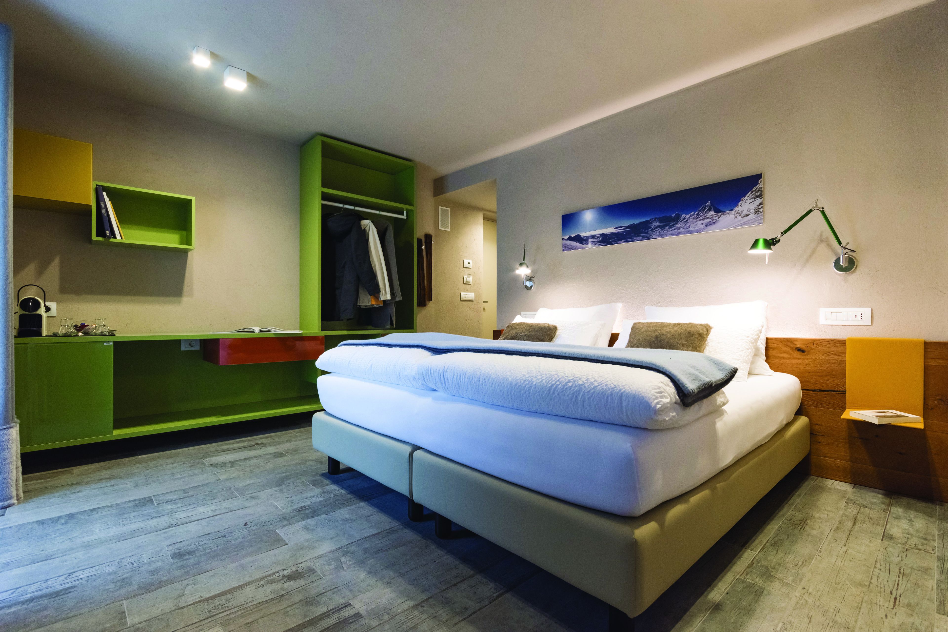 Ein modernes Schlafzimmer mit einem großen Bett, integriertem grünen Stauraum, einem Nachttisch und einer Wandlampe.