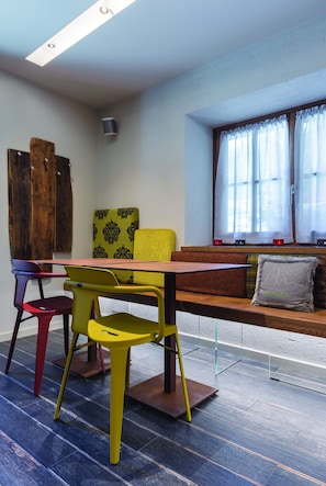 A dining area with a wooden table and benches, colorful chairs, and a window with curtains. - 4478 Mountain Lodge (Valtournenche)