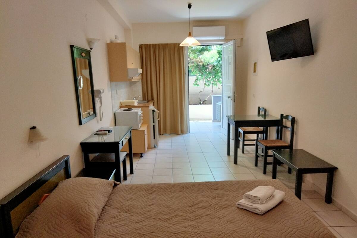 A hotel room with a bed, a desk, a chair, a television, and a bathroom visible through an open door.