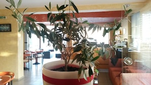A potted plant in a red and white pot on a table in a hotel lobby with orange seating and a bar area in the background. - Zannis Hotel (Rethymno)