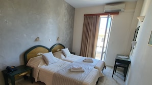 A hotel room with two beds, a bedside table with a phone, a small table with papers, and a view of the outside through a window with curtains. - Zannis Hotel (Rethymno)