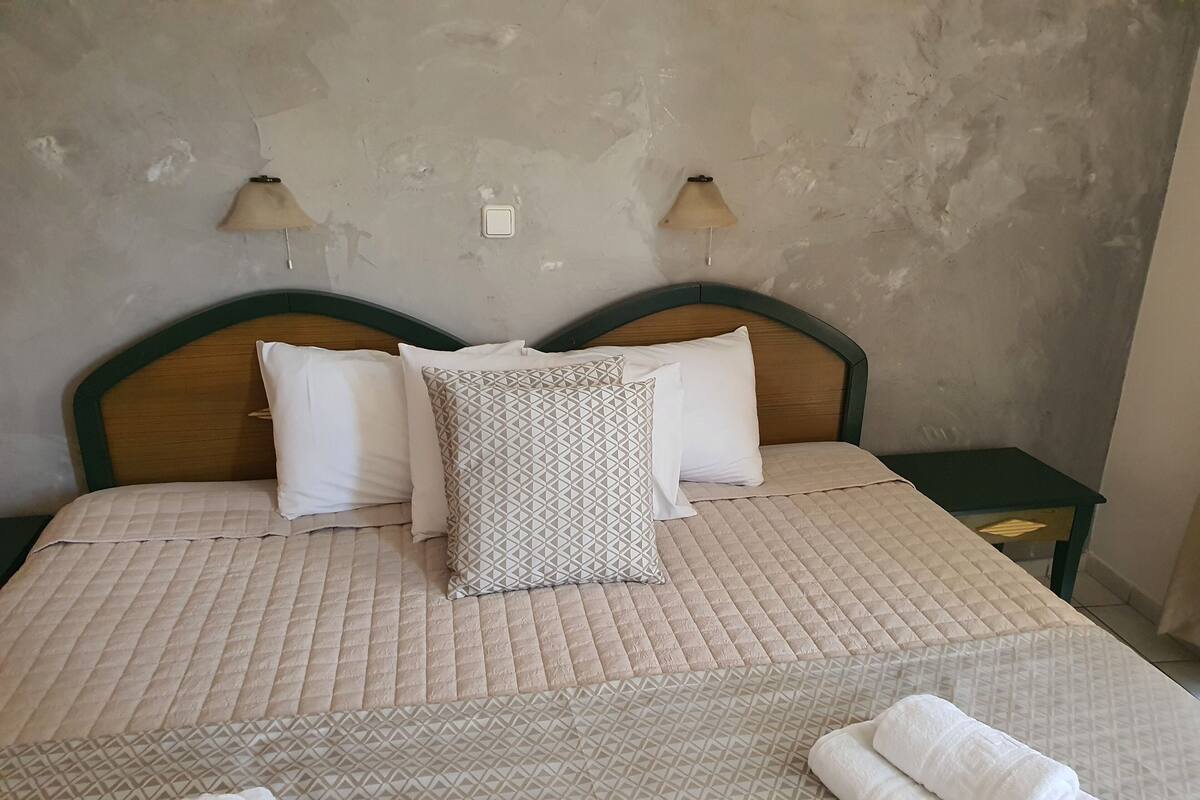 A bed with a quilted beige cover, two bedside tables, and a patterned pillow.