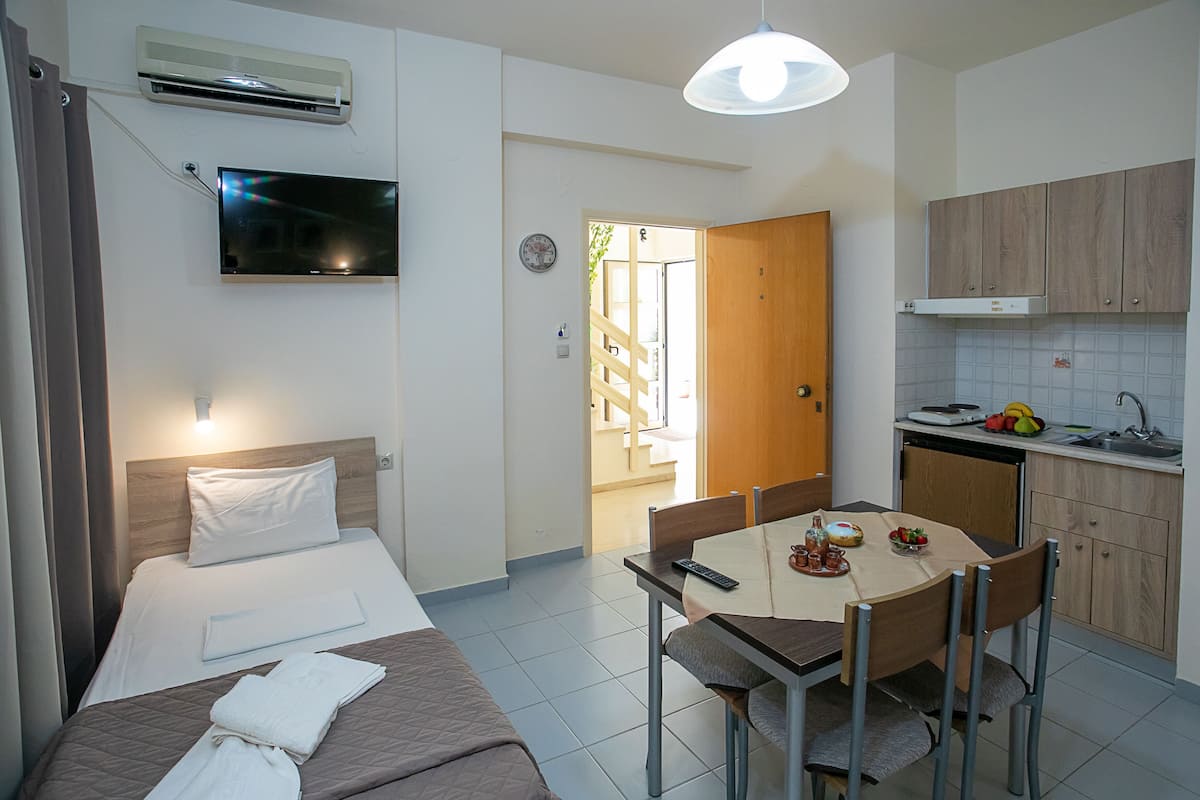 Habitación de hotel con cama, mesita de noche, televisión y una pequeña cocina americana con fregadero y armarios.