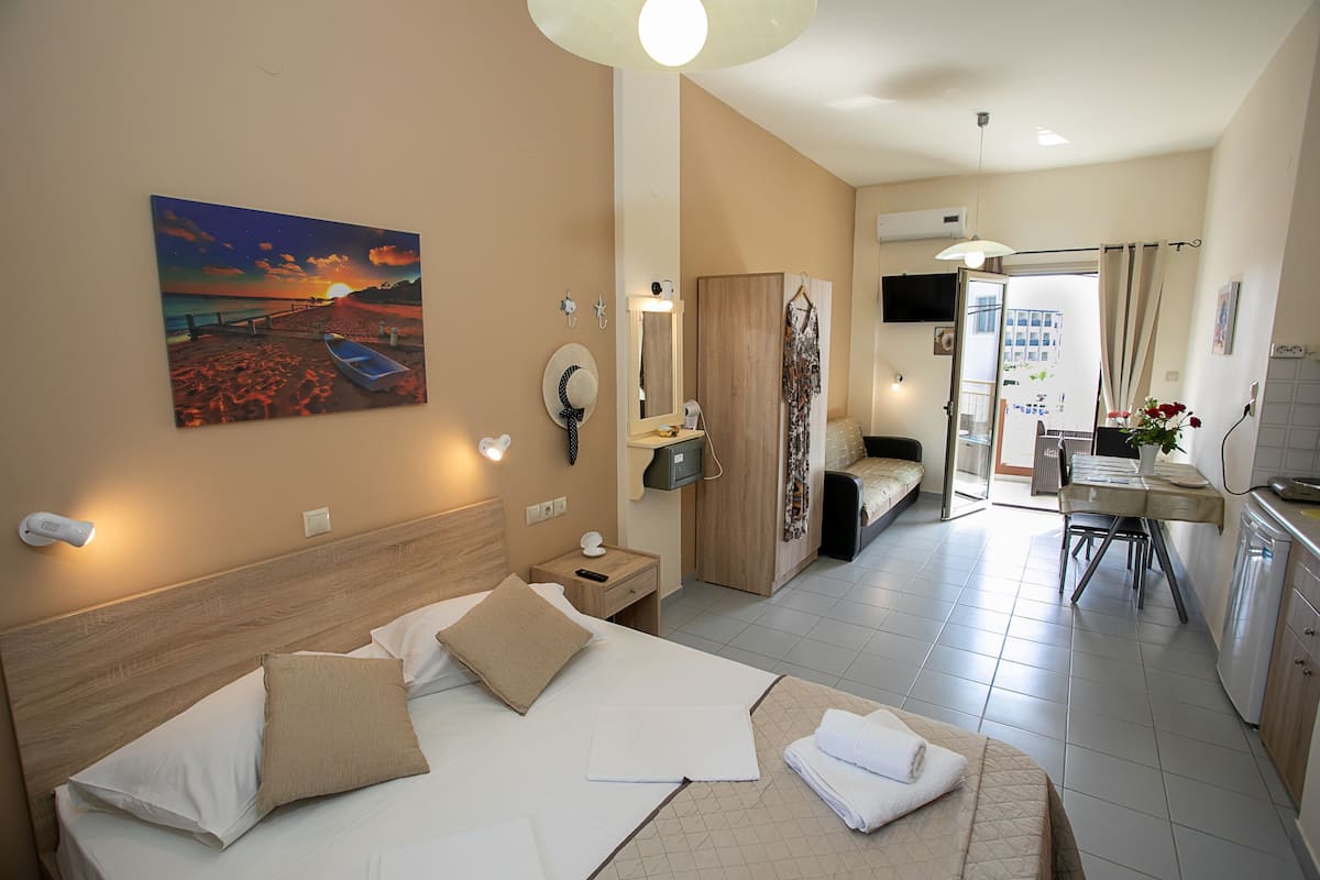 Habitación de hotel con cama, escritorio, silla, espejo y un cuadro de una playa.