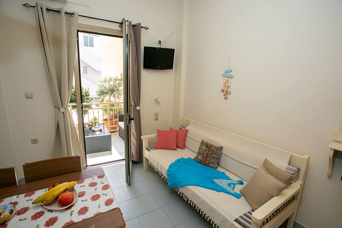 Una habitación con cama, televisión, mesa de comedor y frutas, y vista al exterior.