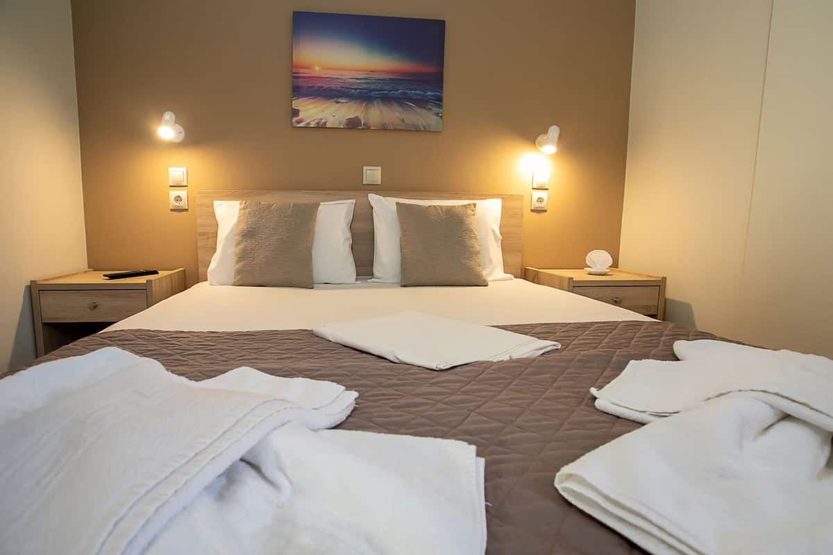 Habitación de hotel con una cama, dos mesitas de noche, un cuadro en la pared y vista al mar.