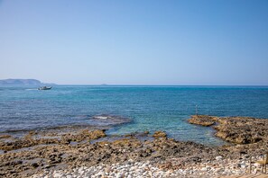 Un rivage rocheux bordé d’une eau d’un bleu limpide, un bateau à l’horizon et une petite île en arrière-plan.