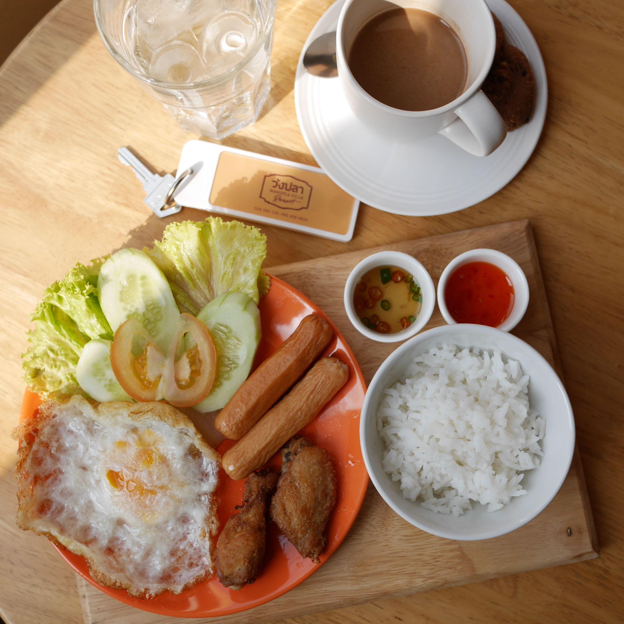 A meal with rice, fried egg, vegetables, and sauces on a wooden table.