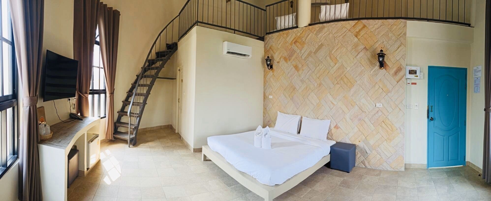 Habitación de hotel con cama, escalera, aire acondicionado instalado en la pared, puerta azul y pared con patrón de espiga.